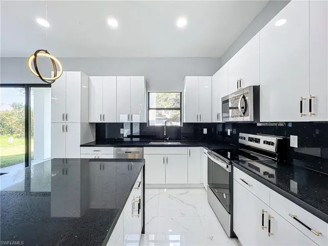 Kitchen with sink, white cabinetry, stainless steel appliances, decorative light fixtures, and dark stone countertops