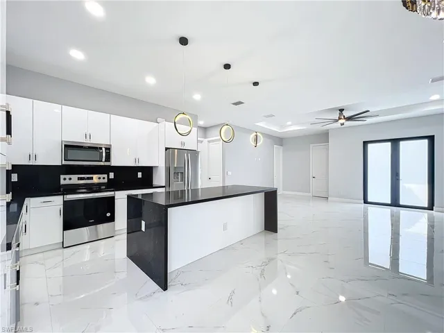 Kitchen with decorative backsplash, hanging light fixtures, stainless steel appliances, a center island, and white cabinets