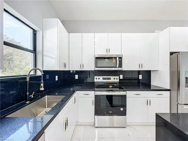 Kitchen with tasteful backsplash, appliances with stainless steel finishes, sink, white cabinets, and dark stone countertops