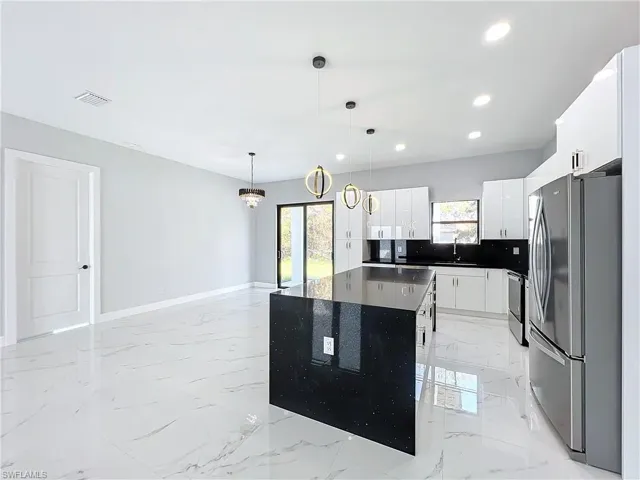 Kitchen featuring white cabinets, stainless steel appliances, decorative light fixtures, and a wealth of natural light