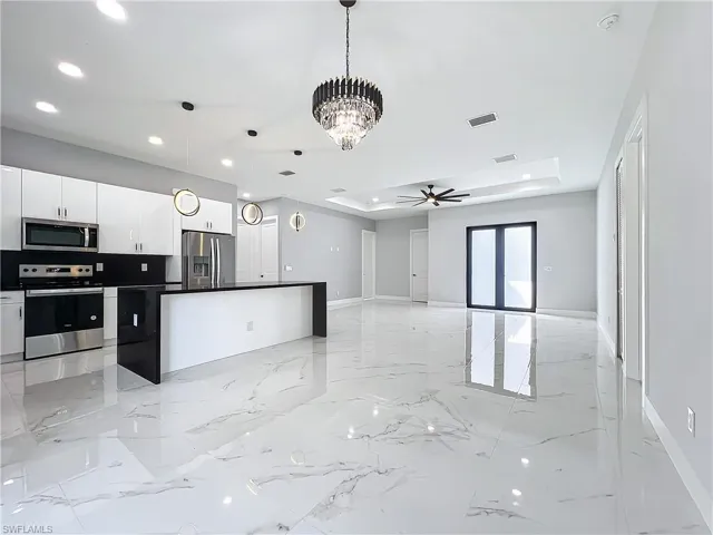 Kitchen with ceiling fan with notable chandelier, a raised ceiling, stainless steel appliances, decorative light fixtures, and white cabinets