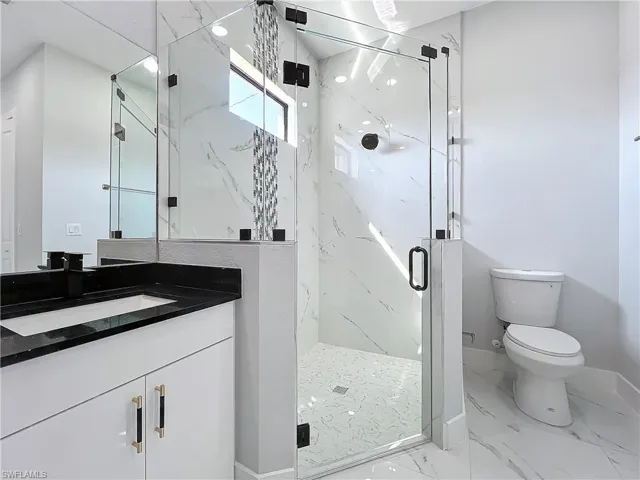Bathroom featuring a shower with door, toilet, and vanity