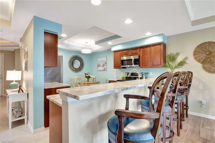 Kitchen with appliances with stainless steel finishes, kitchen peninsula, a breakfast bar area, ornamental molding, and a tray ceiling
