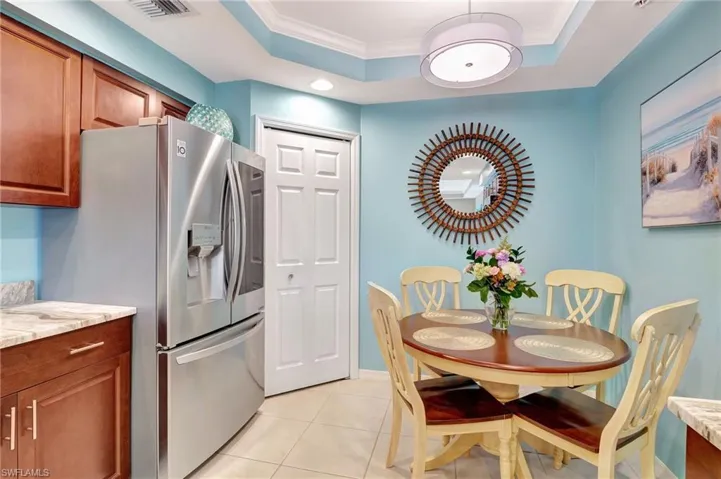 Kitchen featuring ornamental molding, stainless steel fridge with ice dispenser, light tile patterned floors, and a tray ceiling