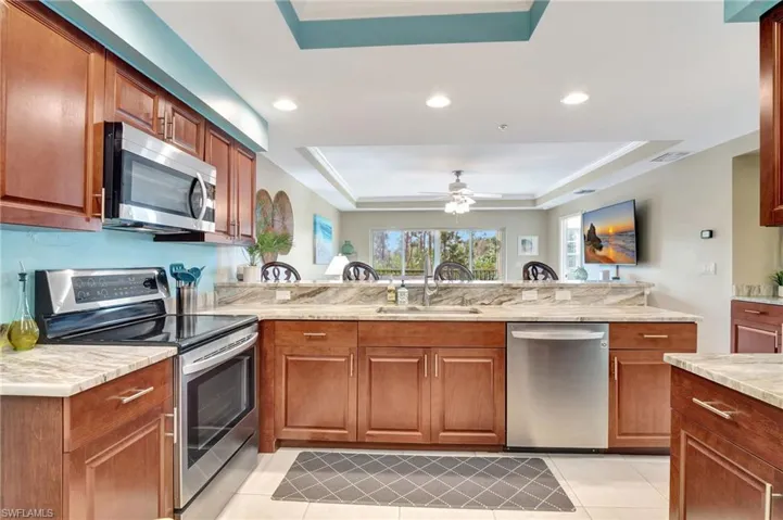 Kitchen with stainless steel appliances, sink, light stone counters, and a tray ceiling