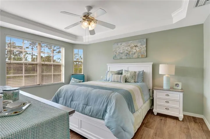 Bedroom with a raised ceiling, wood-type flooring, crown molding, and ceiling fan