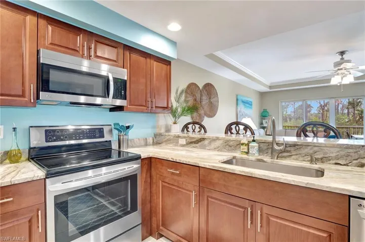 Kitchen with appliances with stainless steel finishes, sink, light stone counters, ceiling fan, and a raised ceiling