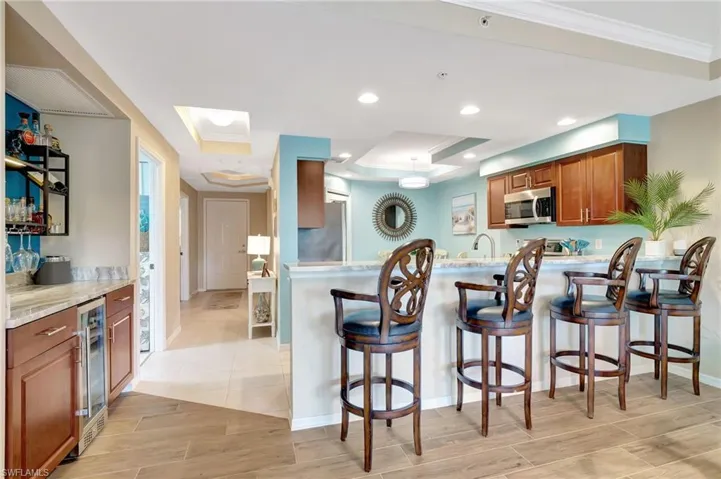 Kitchen with wine cooler, a breakfast bar, sink, ornamental molding, and light stone countertops