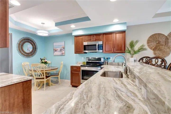 Kitchen with light stone countertops, appliances with stainless steel finishes, sink, and a tray ceiling