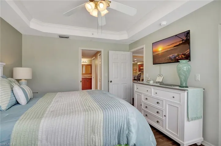 Bedroom with connected bathroom, ornamental molding, a raised ceiling, and ceiling fan
