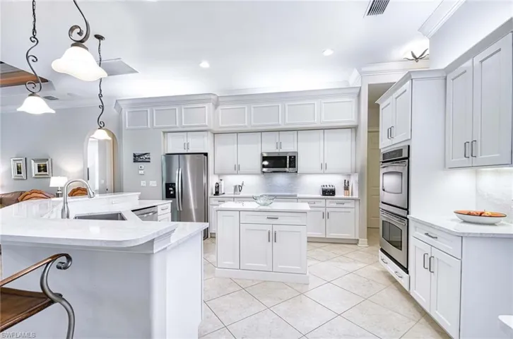 Kitchen featuring crown molding, arched walkways, hanging light fixtures, white cabinets, and appliances with stainless steel finishes