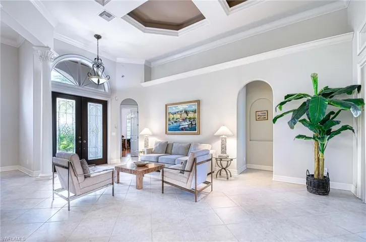 Living area with a high ceiling, arched walkways, french doors, ornamental molding, and coffered ceiling