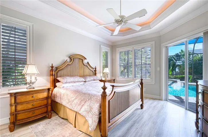 Bedroom featuring wood finished floors, a tray ceiling, access to exterior, ceiling fan, and crown molding
