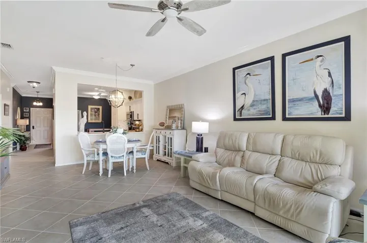Tiled living room featuring ornamental molding, visible vents, and ceiling fan with notable chandelier