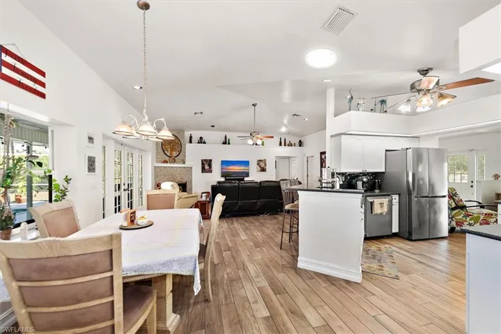 Dining room featuring light wood-type flooring, a ceiling fan, a fireplace, high vaulted ceiling, and recessed lighting