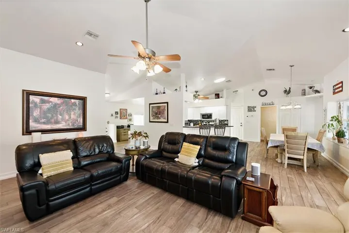 Living room with lofted ceiling, a ceiling fan, light wood-type flooring, recessed lighting, and a chandelier