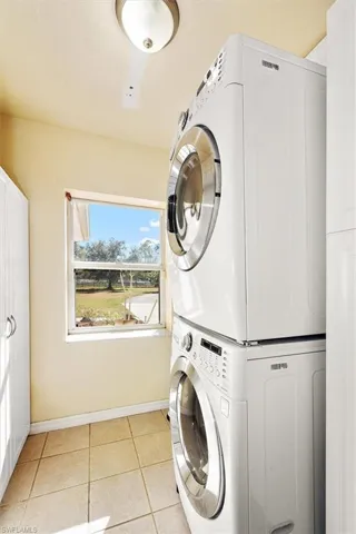 Laundry room with light tile patterned flooring and stacked washer / dryer