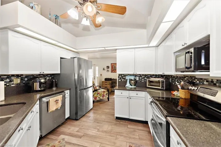 Kitchen with appliances with stainless steel finishes, tasteful backsplash, light wood-style floors, and white cabinetry