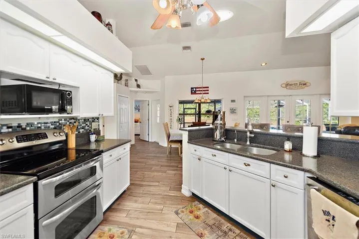 Kitchen featuring stainless steel appliances, white cabinetry, ceiling fan, hanging light fixtures, and dark stone counters