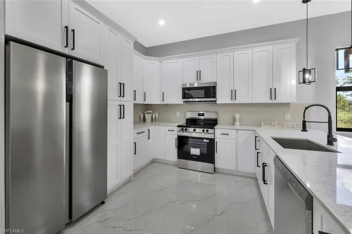 Kitchen featuring stainless steel appliances, pendant lighting, white cabinetry, light stone counters, and light marble finish floors