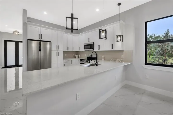 Kitchen with stainless steel appliances, light stone counters, a peninsula, white cabinets, and light marble finish flooring