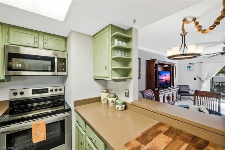 Kitchen with green cabinetry, stainless steel appliances, open shelves, ornamental molding, and ceiling fan