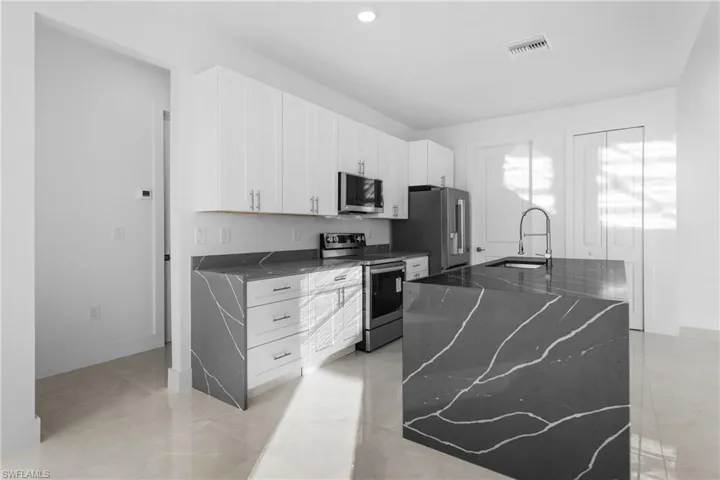 Kitchen with sink, a center island, dark stone countertops, appliances with stainless steel finishes, and white cabinets