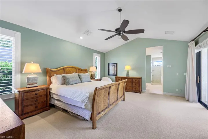 Carpeted bedroom featuring vaulted ceiling, ceiling fan, and ensuite bathroom