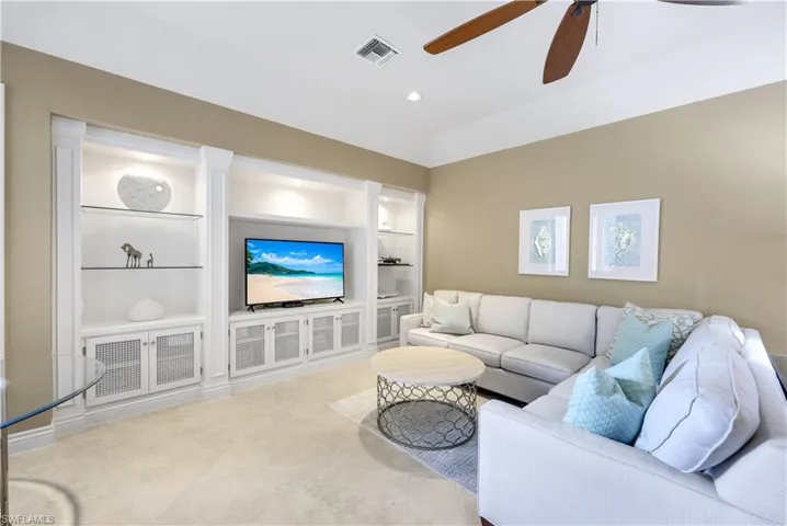 Living room with light tile patterned floors, built in shelves, and ceiling fan