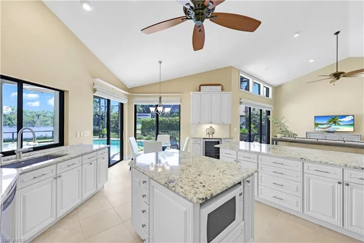 Kitchen with sink, white cabinets, vaulted ceiling, ceiling fan, and white microwave