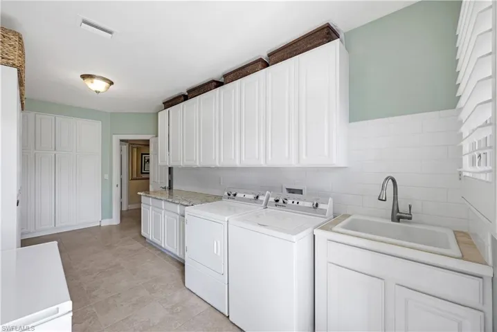 Laundry room featuring separate washer and dryer, sink, light tile patterned floors, and cabinets