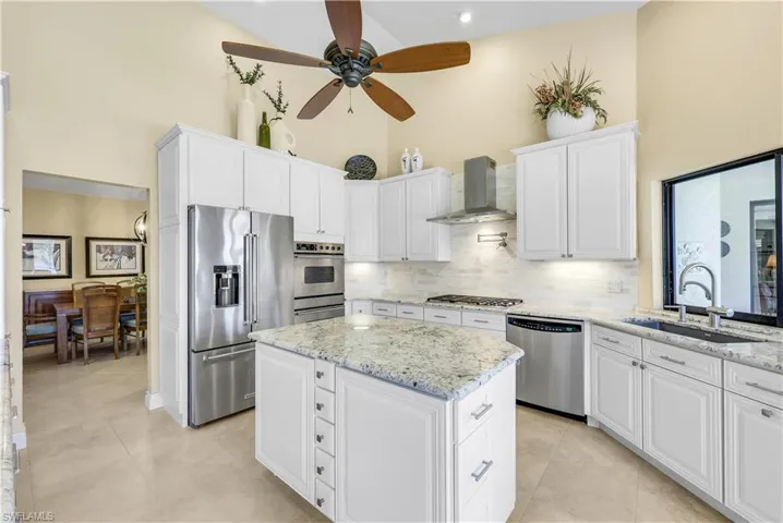 Kitchen featuring appliances with stainless steel finishes, high vaulted ceiling, wall chimney exhaust hood, ceiling fan, and sink