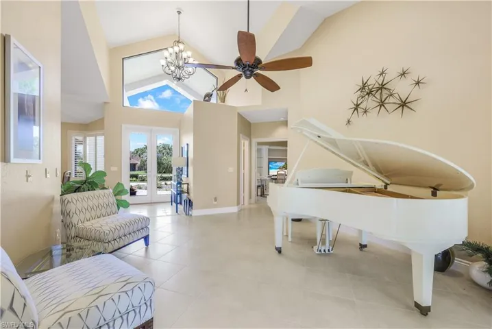 Sitting room with ceiling fan with notable chandelier, light tile patterned flooring, french doors, and high vaulted ceiling