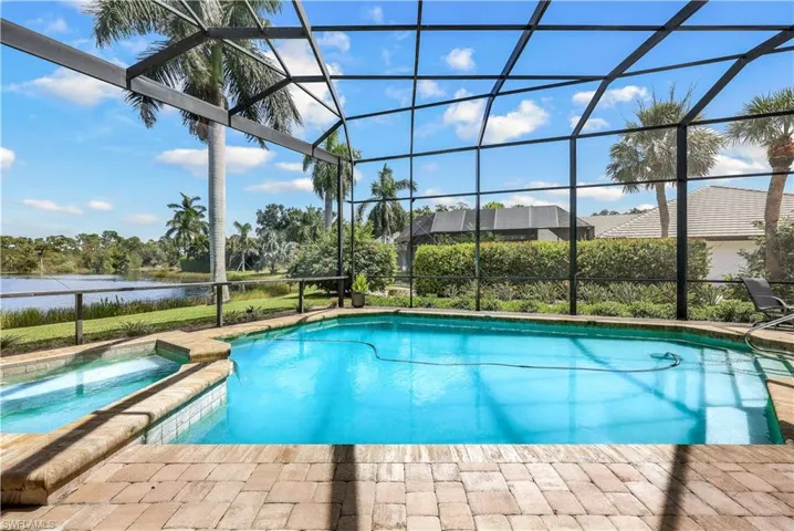 View of pool featuring glass enclosure, a water view, a patio area, and an in ground hot tub
