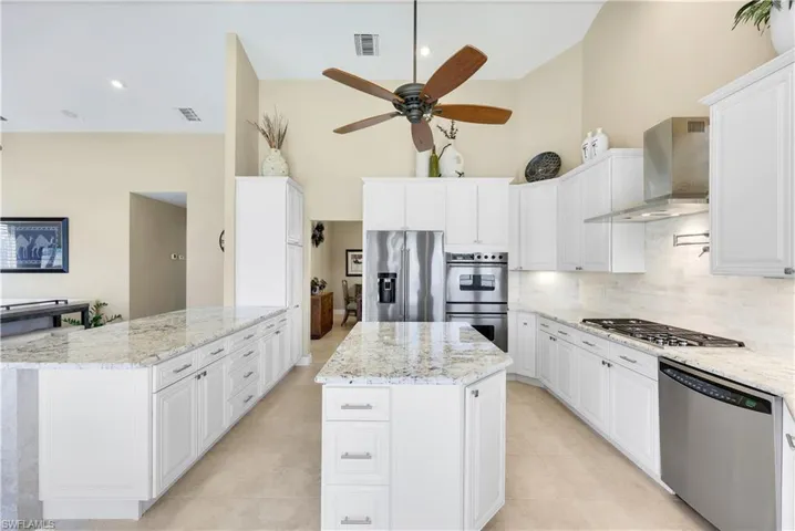 Kitchen featuring light stone counters, stainless steel appliances, wall chimney exhaust hood, and a kitchen island