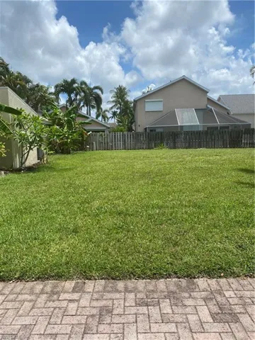 Expansive green lawn with a paver patio border, surrounded by mature tropical foliage