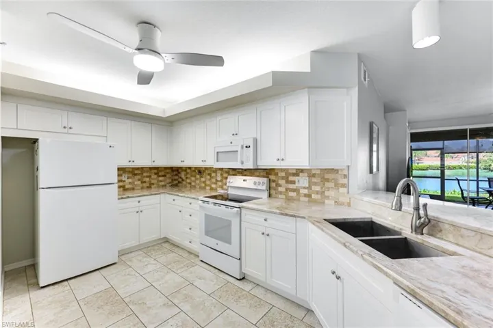 Kitchen with white appliances, backsplash, white cabinets, and light stone counters