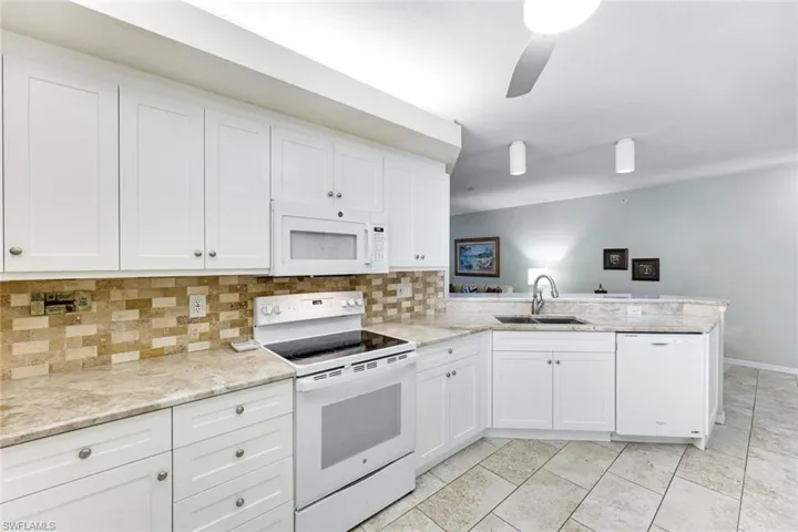Kitchen featuring white appliances, a peninsula, backsplash, and white cabinets