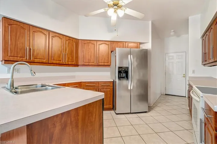 Kitchen with sink, light tile patterned floors, stainless steel fridge, ceiling fan, and white electric range