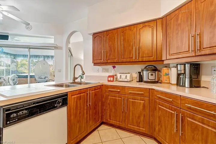 Kitchen featuring light tile patterned flooring, kitchen peninsula, dishwasher, ceiling fan, and sink