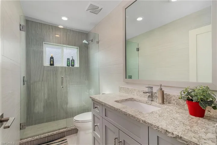 Bathroom featuring tile walls, vanity, toilet, a stall shower, and visible vents