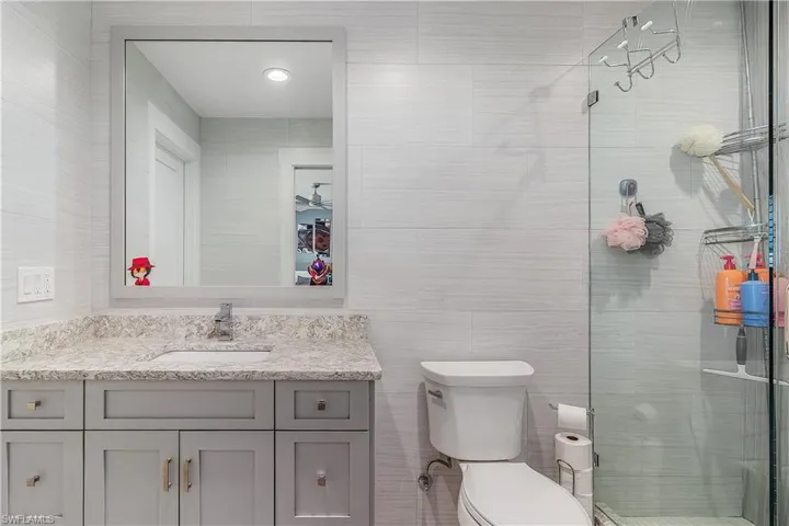 Bathroom with vanity, toilet, a stall shower, and tile walls
