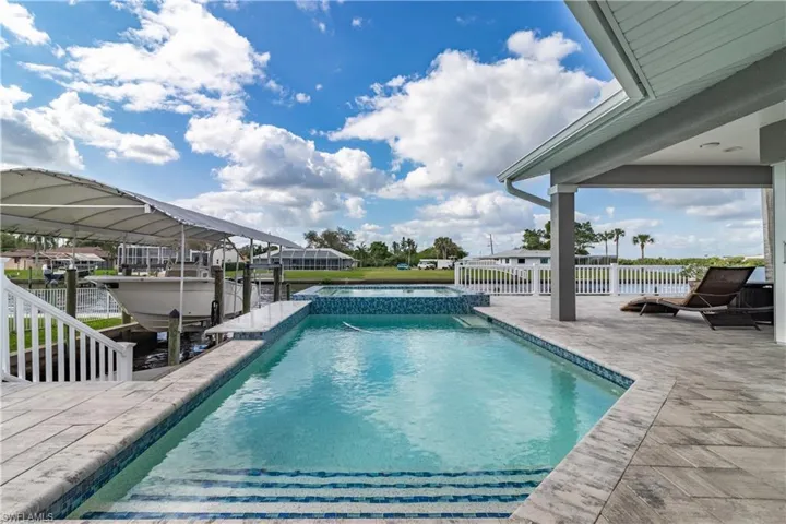 View of pool featuring boat lift, a patio area, fence, a dock, and a pool with connected hot tub