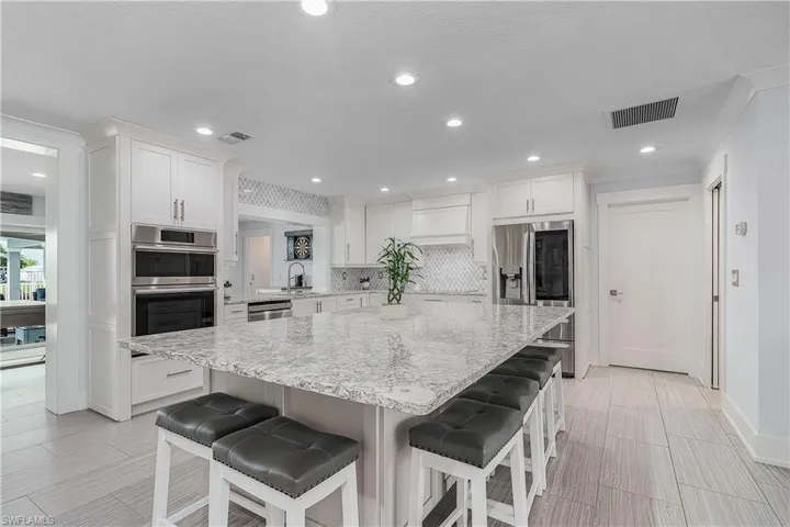 Kitchen with stainless steel appliances, a breakfast bar area, backsplash, a kitchen island, and white cabinets