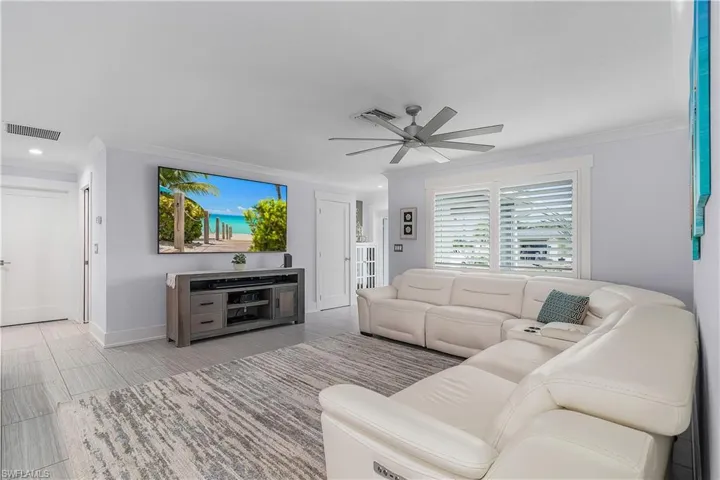 Living room with crown molding, visible vents, ceiling fan, and baseboards