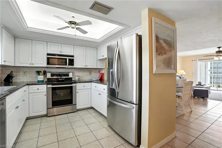 Kitchen featuring ceiling fan, stainless steel appliances, light tile patterned floors, tasteful backsplash, and white cabinets - Virtually Edited Image