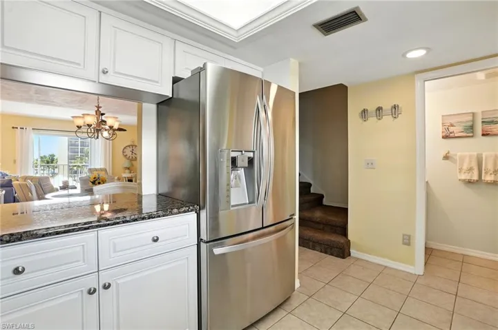 Kitchen featuring stainless steel fridge with ice dispenser, light tile patterned flooring, white cabinets, dark stone countertops, and a chandelier - Virtually Edited Image