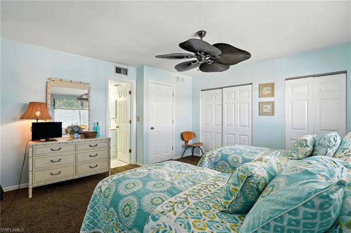 Bedroom featuring dark colored carpet, multiple closets, and a ceiling fan - Virtually Edited Image