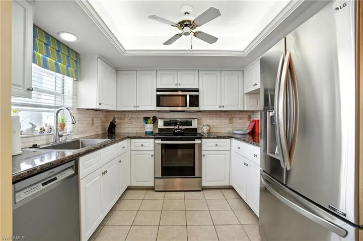 Kitchen featuring stainless steel appliances, a raised ceiling, tasteful backsplash, and light tile patterned flooring - Virtually Edited Image