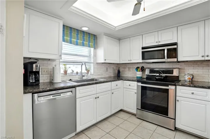 Kitchen with stainless steel appliances, light tile patterned floors, a raised ceiling, tasteful backsplash, and white cabinets - Virtually Edited Image